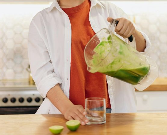 Personne versant un smoothie vert dans un verre, sur un plan de cuisine.