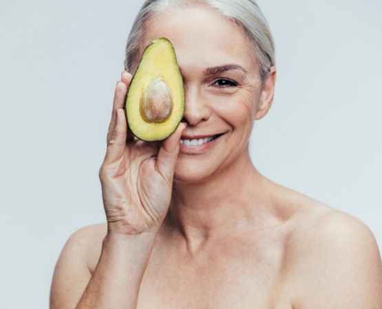 Femme souriante tenant un avocat devant son visage, sur fond neutre.