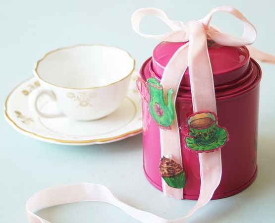 Three brooches decorated in coloured plastic with cake and teapot motifs.