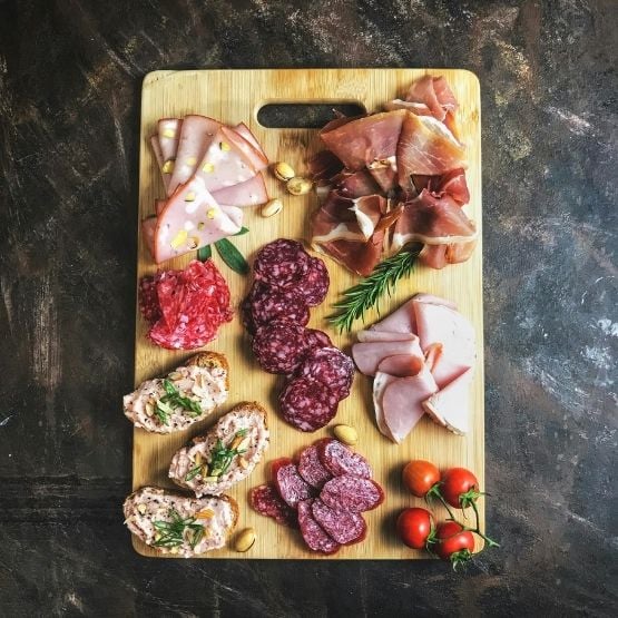 Planche en bois garnie de charcuteries variées, tomates cerises et tartinades.