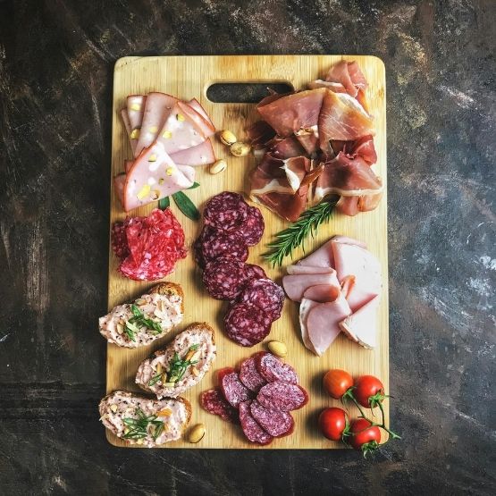 Wooden board with a variety of cold meats, cherry tomatoes and spreads.
