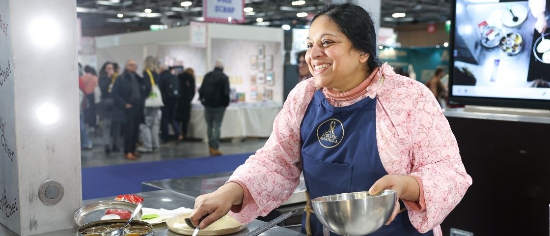 Cheffe souriante réalisant une démonstration de cuisine sur un stand, entourée de visiteurs