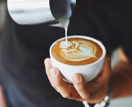 Réalisation d’un latte art en forme de feuille dans une tasse de café, gros plan sur le geste du barista