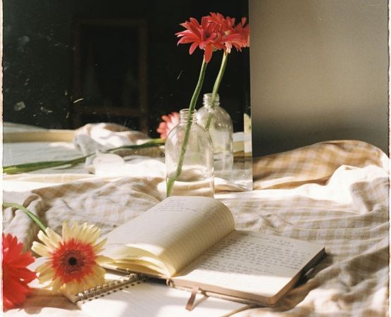Carnet ouvert posé sur un lit avec des fleurs dans des bouteilles en verre, ambiance journaling poétique.