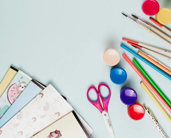Fournitures de loisirs créatifs colorées avec carnets, pinceaux, ciseaux et peinture sur fond clair.