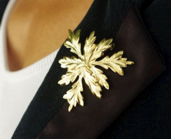 Broche dorée en forme de feuille fixée sur un vêtement noir, illustrant un travail artisanal raffiné.