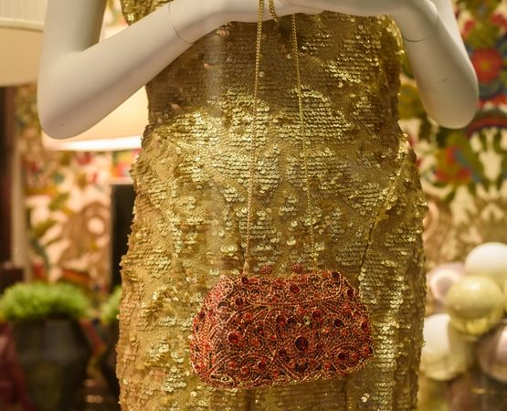 Mannequin portant une robe dorée ornée d’une pochette artisanale suspendue, mise en scène élégante autour de l’or.