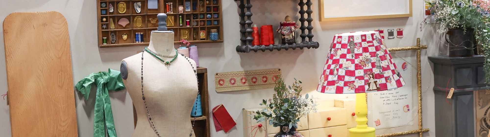 Atelier de creation avec mannequin de couture, objets decoratifs vintage, etagere murale et lampe coloree dans un espace artisanal.