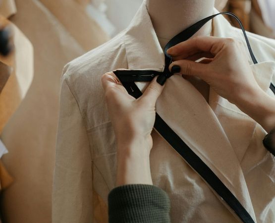 Broderie realisee a la main sur le col d’une veste beige lors d’un travail artisanal textile.