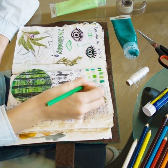 Hand colouring an art journal filled with drawings, collages and creative notes.