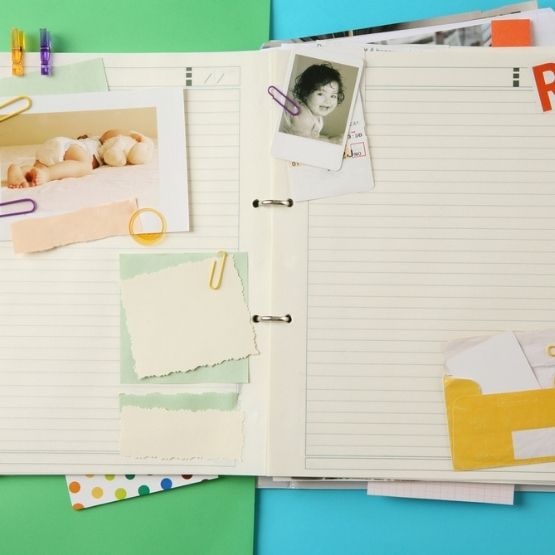 Open notebook with photos, coloured paper and notes attached with paper clips.