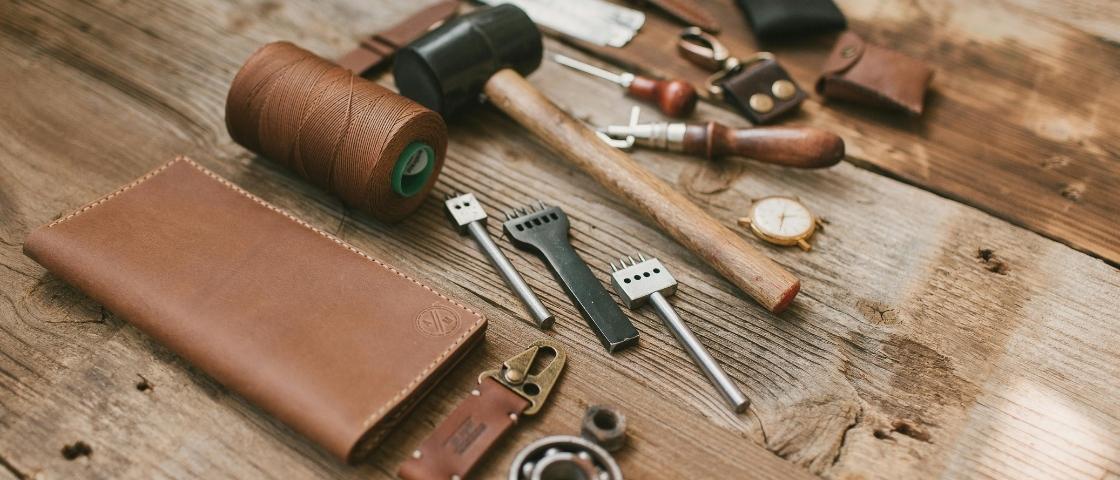 Outils de travail du cuir et portefeuille sur table en bois.