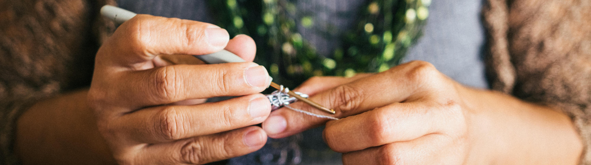 Hands crocheting with a silver metallic thread on a wooden table.