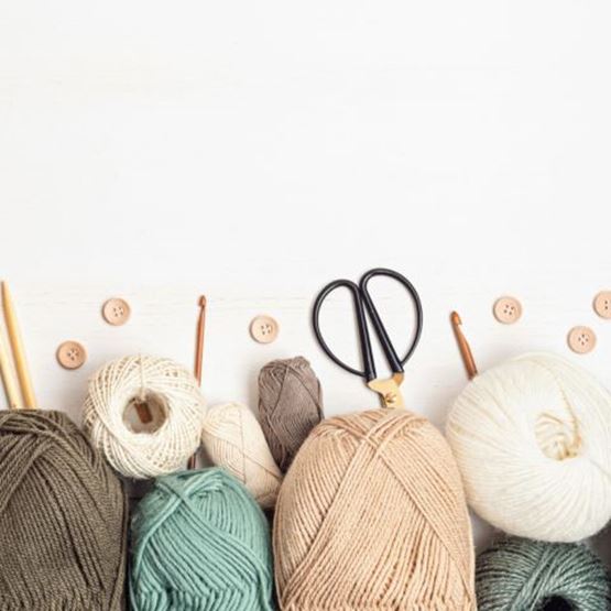 Basket containing balls of natural wool and a piece being knitted with needles.