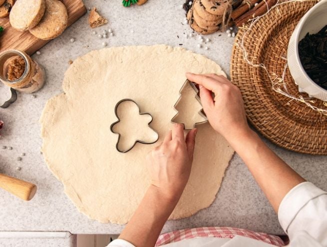 Main découpant des formes de biscuits de Noël dans une pâte avec des emporte-pièces.