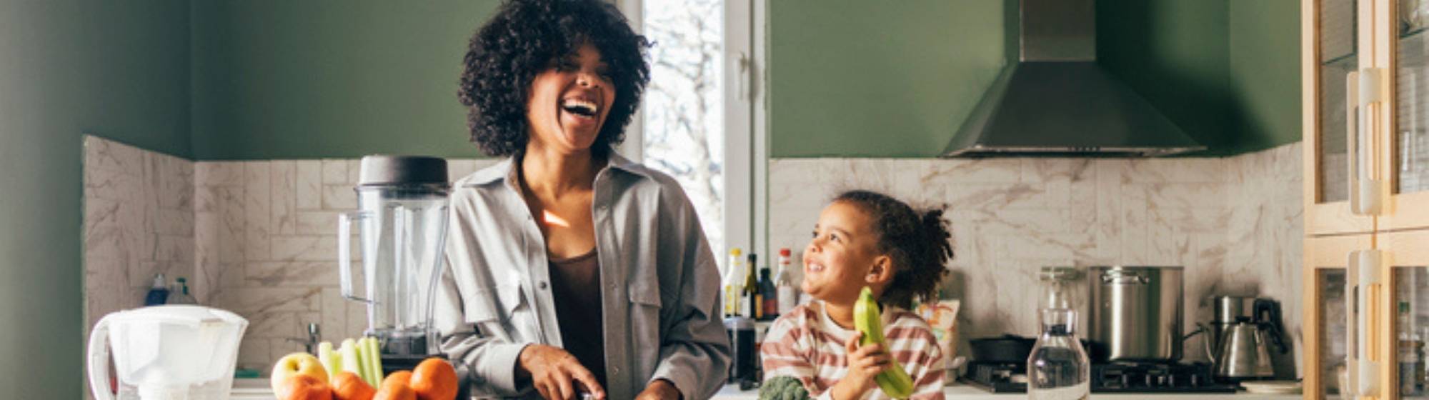 Mère et enfant préparant des légumes ensemble dans une cuisine lumineuse, en souriant.