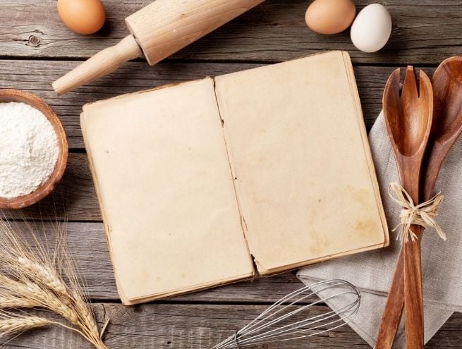 Carnet de recettes ancien ouvert avec ustensiles et ingrédients de cuisine autour.