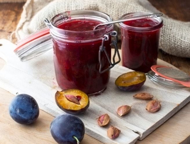 Pots de confiture de prunes maison posés sur une planche avec des prunes fraîches.