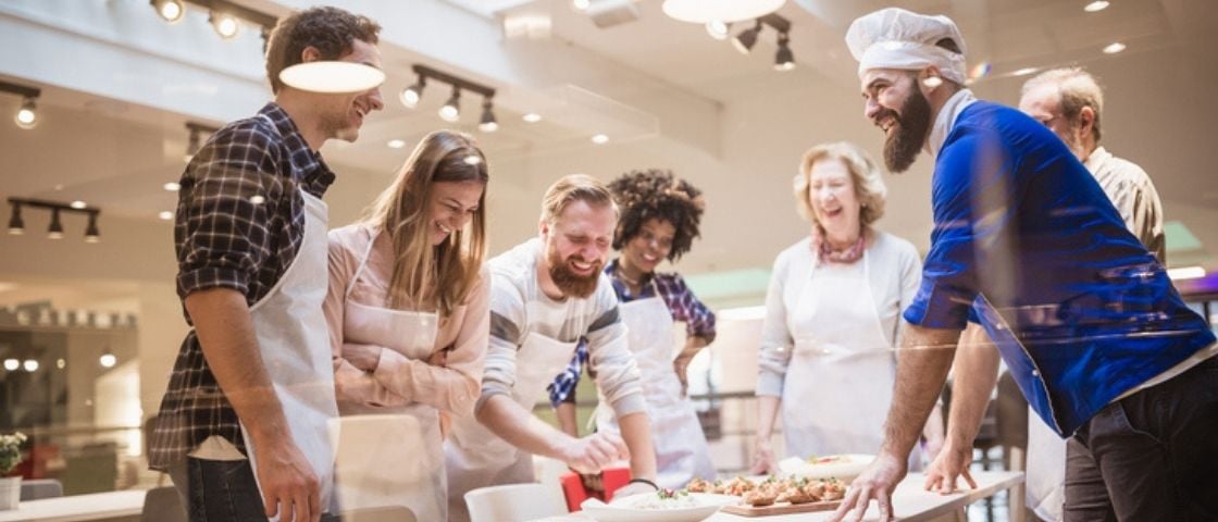 Groupe de personnes participant à un atelier de cuisine et riant autour d’un plan de travail.