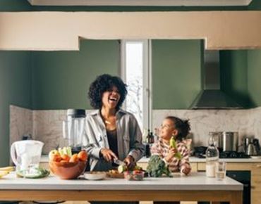 Mère et enfant préparant des légumes ensemble dans une cuisine lumineuse, en souriant.