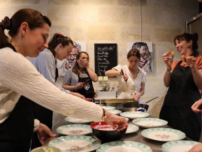 Atelier culinaire avec plusieurs personnes préparant des plats ensemble autour d’un plan de travail.