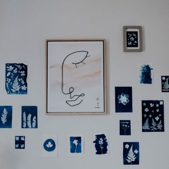A wall display of blue and white cyanotype works around a framed minimalist illustration.