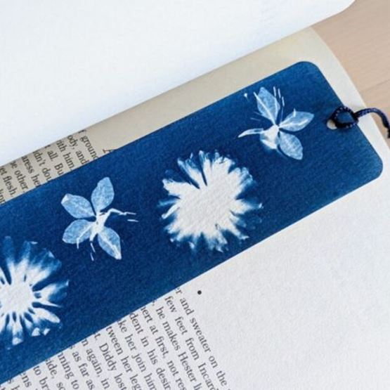 Cyanotype bookmark inserted in a book, decorated with white plant motifs on a blue background.