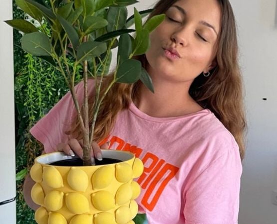 Femme tenant un cache-pot jaune texturé avec une plante verte dans un univers déco DIY