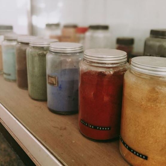 Jars containing different coloured natural pigments lined up on a shelf.