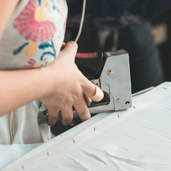Person using a wall stapler on a white fabric.