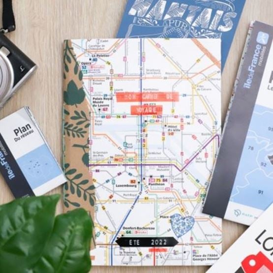 Carnet de voyage personnalisé posé sur un plan de métro parisien, entouré de guides et d’accessoires touristiques.