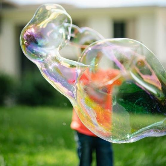 Giant soap bubbles in front of a blurred child in the background in a garden.