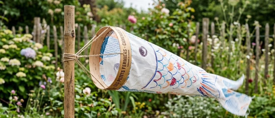 Manche à air illustrée représentant un poisson coloré accroché à un poteau dans un jardin