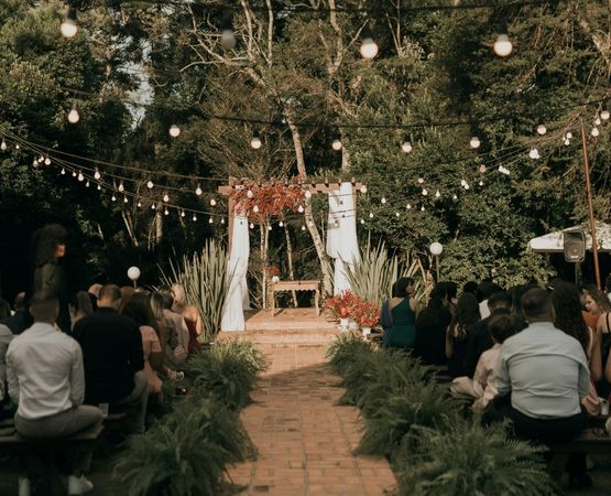 arche ceremonie mariage champetre exterieur fleurs guirlandes lumineuses allee invites