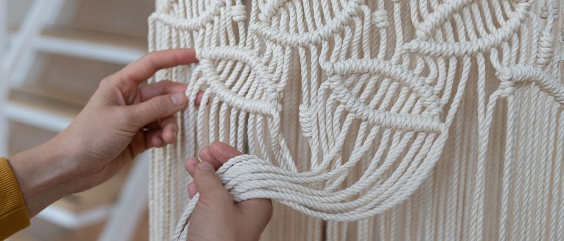 Hands making a macramé with white rope and geometric motifs.