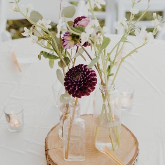 Glass vases with fresh flowers placed on a slice of wood as a centrepiece.