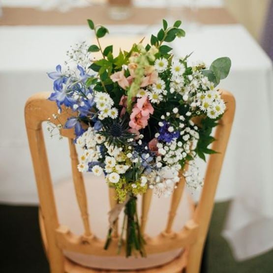 Bouquet champêtre attaché au dossier d’une chaise en bois pour un mariage.