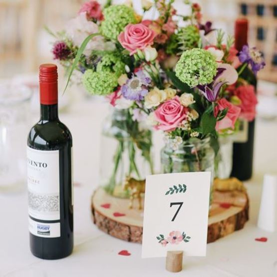 Wedding table centrepiece with fresh flowers, bottle of wine and table number.