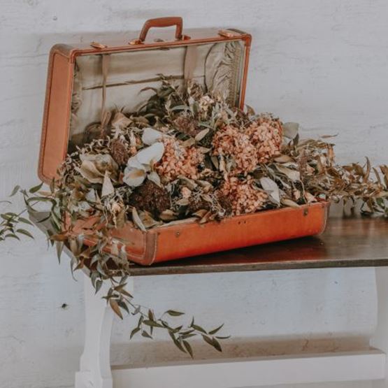 An old orange suitcase full of dried flowers on a rustic table.