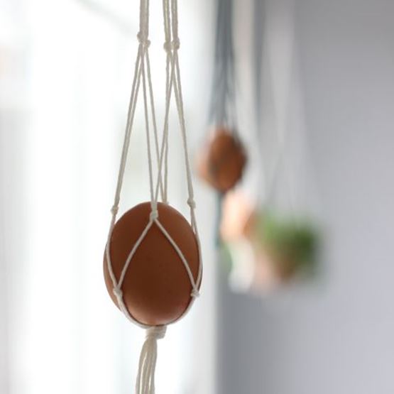 Egg suspended in a white macramé net, hung in front of a window.