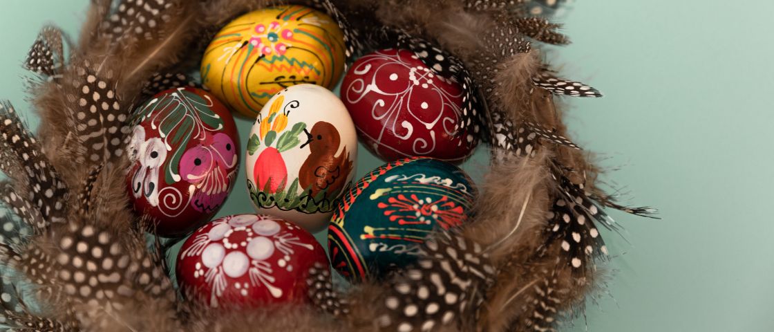 Œufs de Pâques richement décorés posés dans un nid entouré de plumes.