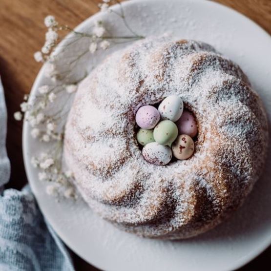 A crown-shaped Easter cake sprinkled with icing sugar and topped with pastel chocolate eggs in the centre.