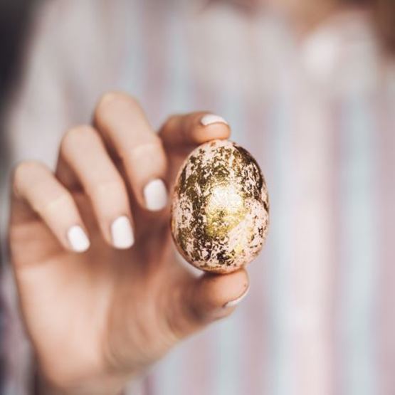 Female hand holding an Easter egg decorated with gold leaf.