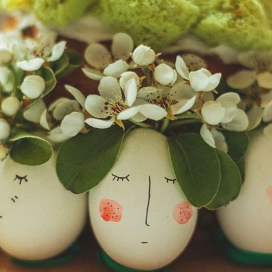 Eggs painted with faces and decorated with green leaves and white flowers as headdresses.