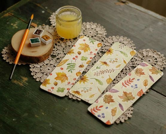 Illustrated bookmarks with handmade floral motifs, placed on a wooden table with creative materials.