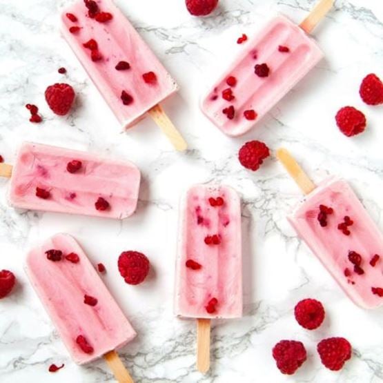 Glaces à l’eau roses avec morceaux de framboises, posées sur fond marbré.