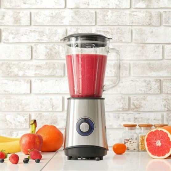 Blender containing a red smoothie, surrounded by fresh fruit.