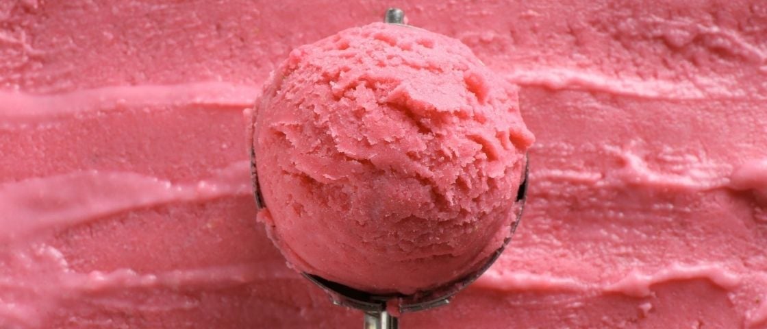 A large ball of pink sorbet placed on a surface of spread sorbet.