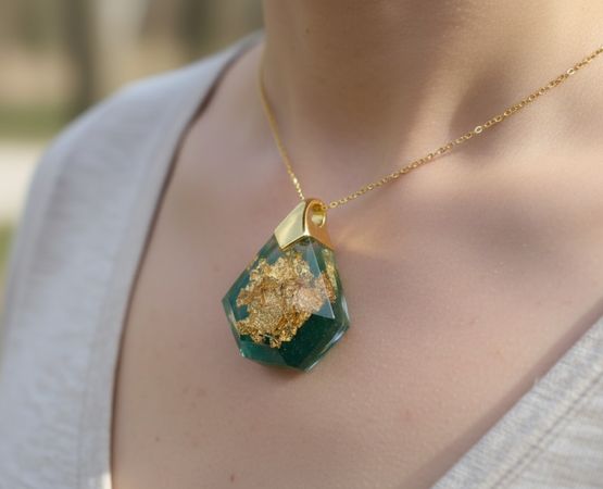 Collier artisanal avec pendentif vert incrusté de feuilles d’or, porté autour du cou.