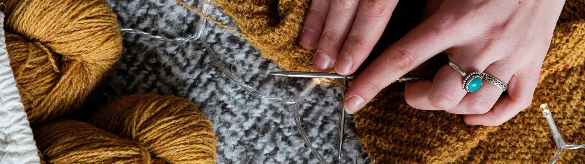 Mains en train de tricoter avec des pelotes de laine marron et des aiguilles